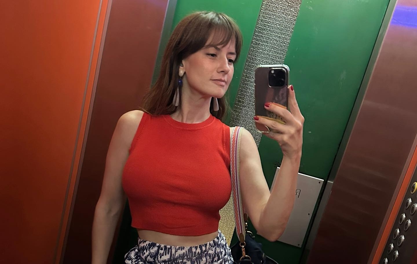 Altair Jarabo poses in an elevator wearing a tight red top and patterned shorts