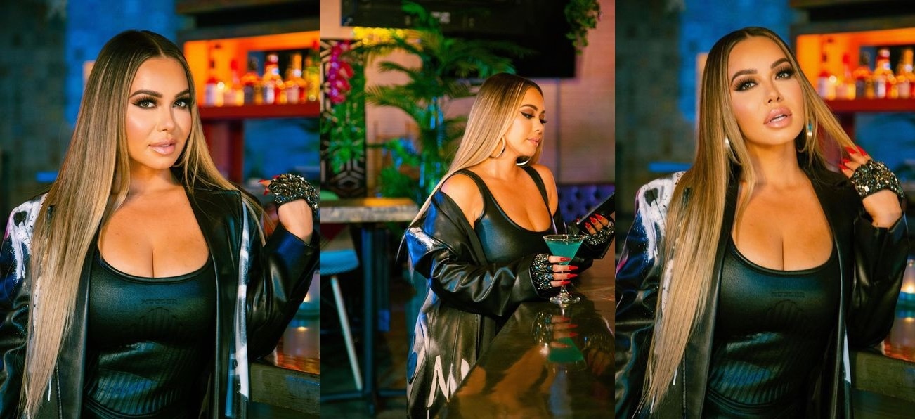 Wearing a black vinyl minidress Chiquis Rivera shows off her figure and poses in a bar